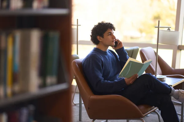 携帯電話で話す大学生で試験の準備をして図書館のキャンパスにあるアームチェアに座っています Knowledge Education — ストック写真