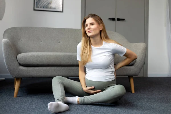 若い妊婦の床に座って 彼女の腹に触れると 首の痛みを感じている 妊娠概念 — ストック写真