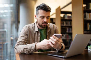 Yakışıklı sakallı öğrenci masada oturuyor, akıllı telefon kullanıyor, internetten alışveriş yapıyor, video izliyor ya da mesajları kontrol ediyor. Çekici bir adam dizüstü bilgisayarla masada oturuyor. Çevrimiçi öğrenim kavramı