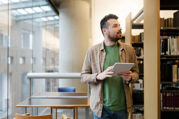 Handsome Man Stands University Library Uses Digital Tablet Looks Away — Stock Photo, Image
