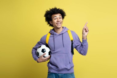 Portrait of young smiling African American man holding ball for soccer game looking at camera isolated on yellow background. Sport, active lifestyle concept 