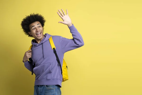 黄色の背景に孤立手を振って スタイリッシュなパーカーを着て陽気フレンドリーな多人種大学の学生 離れて見て幸せな成功した男の肖像画 教育理念 — ストック写真