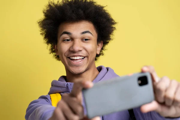 黄色の背景に隔離されたモバイルゲームでセルフィーを作るスマートフォンを使用して陽気なアフリカ系アメリカ人の男 喜びに満ちたヒップスターショッピングオンライン スポーツへの賭け お金を獲得 — ストック写真