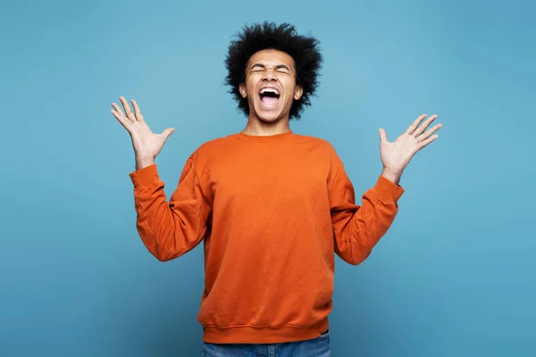 Emotional African American man screaming, rejoicing and feeling overjoyed isolated on blue background. People emotions concept