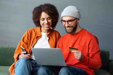 Bir çift gülümseyen arkadaş ellerinde dizüstü bilgisayar, online alışveriş, evdeki kanepede birlikte yemek sipariş ediyorlar. İki başarılı serbest çalışan modern teknolojiyi kullanarak ödeme alıyorlar.
