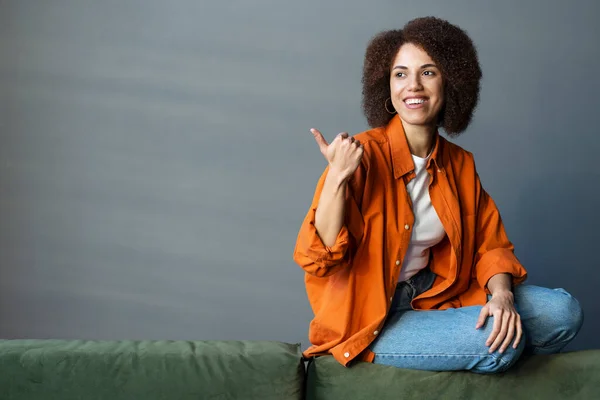 Portret Uśmiechnięta Afroamerykanka Wskazująca Dłoń Przestrzeń Kopiowania Odwracając Wzrok Siedząc — Zdjęcie stockowe