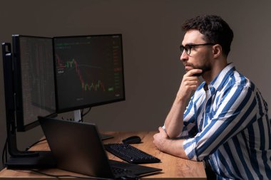 Dalgın yakışıklı adam, bilgisayar monitörüne bakan kripto tüccarı, modern ofiste şifreli çizelgeyle çalışıyor. Borsa araştırmacısı. Başarılı iş, çevrimiçi ticaret kavramı
