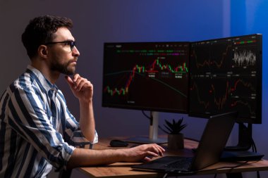 Bilgisayar monitörüne bakan ciddi bir kripto tüccarı, kripto grafiğiyle çevrimiçi çalışıyor modern ofiste oturuyor, pazarı araştırıyor ve analiz ediyor. Çevrimiçi ticaret kavramı