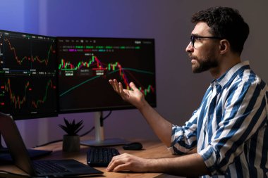 Hüsrana uğramış bir adam, bilgisayar monitörüne bakan bir kripto tüccarı, modern ofiste kripto çizelgesiyle çalışıyor. Çevrimiçi ticaret kavramı