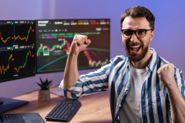 Neşeli yakışıklı tüccar elektronik para kazanıyor, başarıyı kutluyor, evden çalışıyor. Başarılı iş, çevrimiçi ticaret kavramı