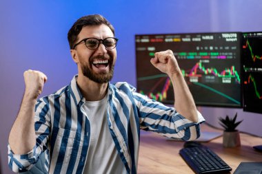 Genç, neşeli kripto tüccarı kutlama başarısını modern ofiste oturarak kutluyor. Başarılı iş, çevrimiçi ticaret kavramı