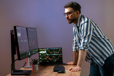 Bilgisayar monitörüne bakan ciddi kripto simsarının gece portresi, kripto grafiği ile çevrimiçi çalışıyor modern ofiste duruyor, pazarı araştırıyor ve analiz ediyor. Teknoloji, çevrimiçi ticaret kavramı