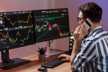 Cep telefonuyla konuşan, bilgisayar monitörüne bakan, modern ofiste kripto çizelgesiyle çalışan şifreli işlemcilerle meşgul. Çevrimiçi ticaret kavramı