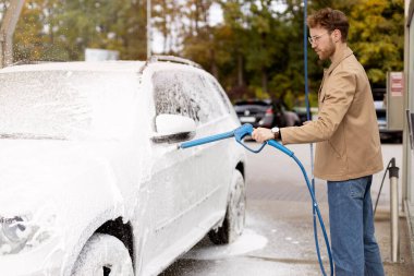 Ciddi bir adam arabasını yüksek basınçlı sabunla sabunluyor. self-servis çamaşır konsepti