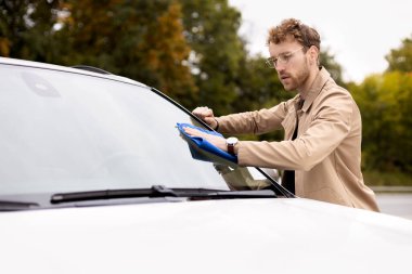 Çekici bir genç adam mikro fiber bezle arabanın ön camını dikkatlice siliyor. Dışarıda araba yıkama, araba yıkama kavramı.