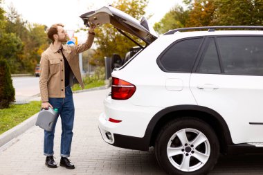 Yakışıklı bir adam arabasının bagajından motor yağı çıkarıyor. Araba servisi konsepti, motor yağı değişimi.