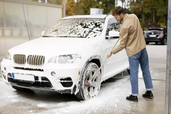 stock image Serious man washing car thoroughly washing wheels with brush. Self service car wash concept
