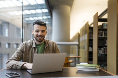 Modern ofiste serbest çalışan dizüstü bilgisayar kullanan gülümseyen İspanyol iş adamının portresi. İş yerinde kameraya bakan mutlu metin yazarı. Başarılı bir iş.