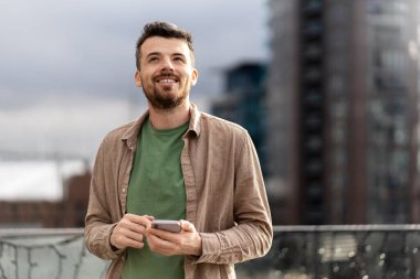 Yakışıklı, orta yaşlı İspanyol bir adam elinde akıllı telefonuyla gezici uygulama alışverişi yapıyor, sokakta yemek sipariş ediyor. Modern hipster adam mesaj atıyor. Mobil bankacılık kavramı