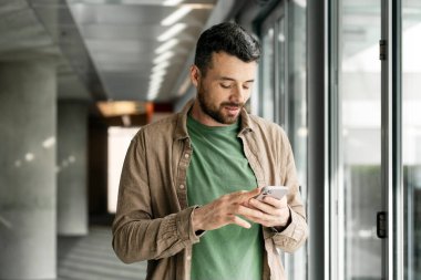 Modern ofiste cep telefonuyla mesaj okuyan çekici orta yaşlı Latin bir adam. Dalgın sakallı hippi akıllı telefonuyla internetten mobil uygulama alışverişi yapıyor ve yemek sipariş ediyor.