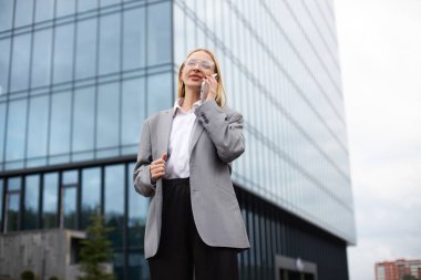 Kendine güvenen orta yaşlı iş kadını şık gözlükler takıyor ve cep telefonuyla sokakta konuşuyor. Teknoloji konsepti
