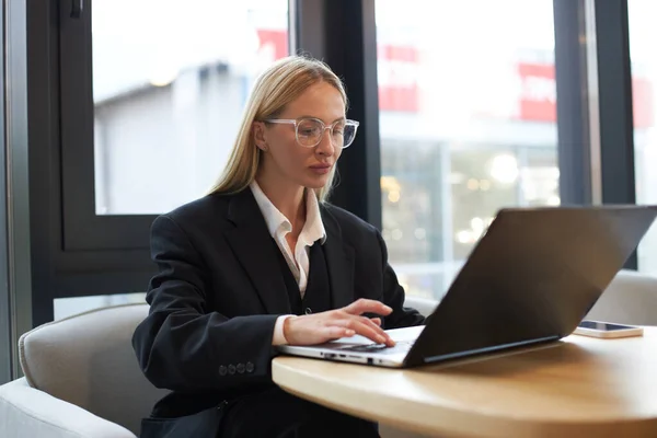 現代のオフィスでオンラインで働くラップトップコンピュータを使用して眼鏡をかけて魅力的なスタイリッシュなビジネス女性 フリーランスのコピーライターがキーボードを入力し 職場でプロジェクトを計画します 成功事業 — ストック写真