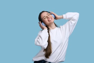 Attractive caucasian brunette woman in wireless headphones, listening to a cool track and moving to music, isolated over blue background. People, dance, hobby, entertainment and lifestyle concept clipart