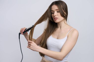 Beyaz tenli güzel bir kadın modern elektrikli saç düzleştirici kullanıyor izole edilmiş beyaz arka planda saçları düzleştiriyor. Profesyonel saç şekillendirme aletleri. Kuaför. Berber. Saç bakımı. Görünüm