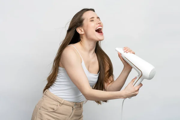 Bellissima Donna Strafelice Usando Asciugacapelli Cantando Divertendosi Isolata Sfondo Bianco — Foto Stock