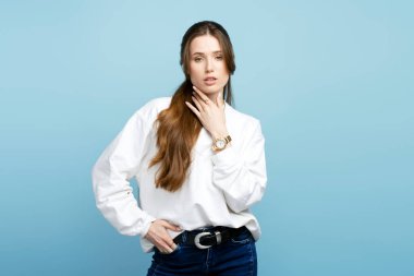 Çekici bir mankenin portresi, güzel uzun saçlı, şık günlük kıyafetler giyen, mavi arka plandaki kameraya bakan. Fotoğraflar için poz veren seksi moda kadını. Doğal güzellik, fotoğraf çekimi. 