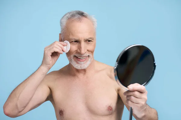 Shirtless Caucasian Senior Man Looking Cosmetic Mirror While Cleaning Face — Stock Photo, Image