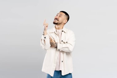 Gülümseyen Koreli genç adam, gri arka planda izole edilmiş bir şekilde fotokopi alanını işaret ediyor. Yakışıklı adam ayakta, şık kıyafetler giyiyor, alışveriş, indirim ve reklam yapıyor.