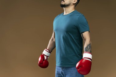 Kahverengi arka planda izole edilmiş egzersiz yapan kırmızı boks eldivenli bir adamın portresi. Yakışıklı sakallı erkek eğitimi, taşınma, hobi.