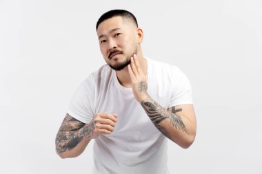 Beyaz arka planda izole bir şekilde aynaya bakarken yüzüne dokunan Koreli yakışıklı adamın yakın plan portresi. Cilt bakımı, temizlik, sabah rutini.