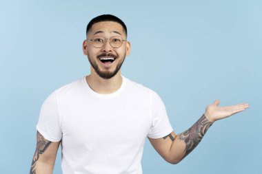 Mavi arka planda izole edilmiş fotokopi alanını gösteren gözlüklü heyecanlı Koreli adam. Alışveriş, satış kavramı