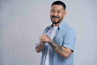 Yakışıklı Koreli sakallı bir adamın portresi, günlük tarz mavi gömlekli, yüzünde pozitif yüz ifadesi olan, gülümseyerek kameraya bakan. Kapalı alanda çekilen çekim gri arka planda izole edildi 