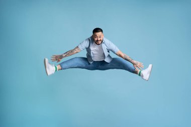 Uzun boylu, neşeli Asyalı bir adam havada bacaklarıyla zıplıyor, enerjik ve hayat dolu hissediyor. Blye arka planda izole edilmiş kapalı stüdyo görüntüleri. 