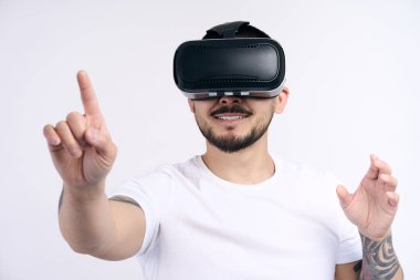 Beyaz tişörtlü genç Koreli adam sanal gerçeklik kulaklığı kullanıyor ve elleri beyaz duvar arkasında video oyunu oynuyor. VR, gelecek, cihazlar, teknoloji konsepti 