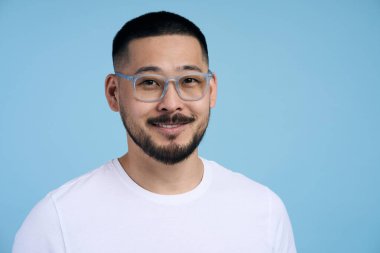 Gözlüklü yakışıklı Asyalı sakallı adamın portresi mutlu bir yüzle poz veriyor, kameraya gülümsüyor. Kahverengi arka planda izole edilmiş neşeli öğrenci. 