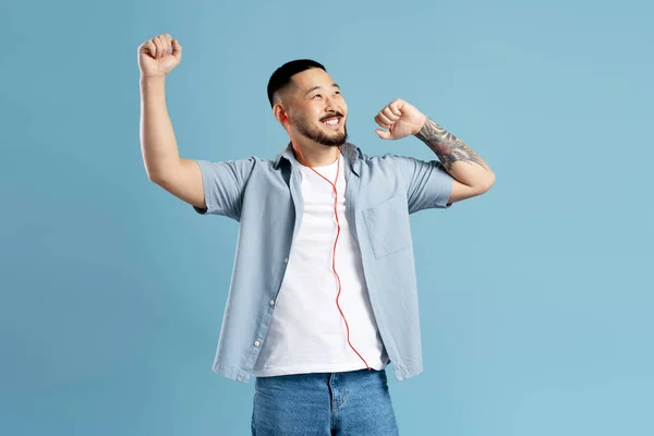 ヘッドフォンを装着したスタイリッシュなタトゥーを持つハンサムな 笑顔アジアの男は 音楽を聞いて 青の背景に隔離されたダンス 現代のテクノロジー ポジティブなライフスタイル — ストック写真
