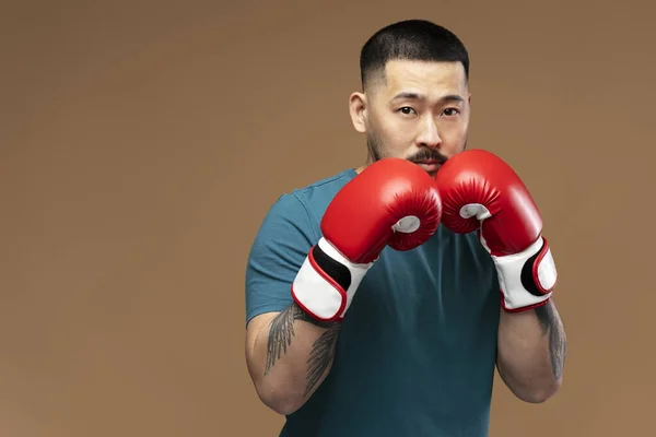 严肃的亚洲男子的画像 戴着红色拳击手套 背景为褐色 复制空间 肌肉发达的年轻拳击手在体育馆的训练 — 图库照片