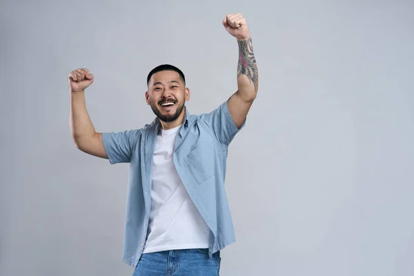興奮した表情で立っている喜びひげを生やしたアジア人の男は 悲鳴を上げ うん叫んで 彼の勝利 成功を祝う 灰色の背景に隔離された屋内スタジオショット — ストック写真