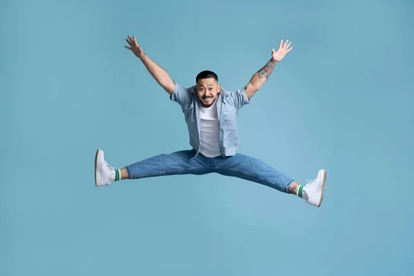 stock image Full length portrait of positive inspired asian man jumping in air. Indoor studio shot isolated on blue background, empty copy space 