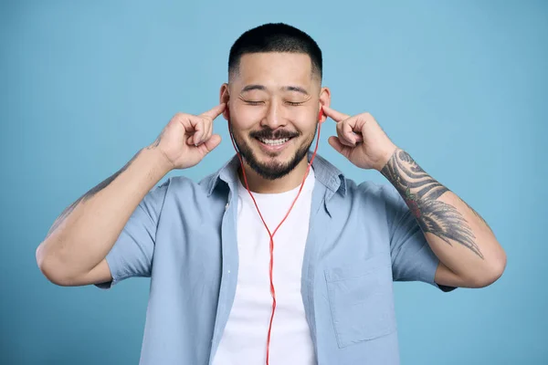 スタイリッシュなタトゥーを持つハンサムな幸せなアジアの男は 青い背景に隔離されたヘッドフォンリスニング音楽を着て スペースをコピーします テクノロジー 肯定的な感情の概念 — ストック写真
