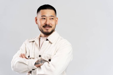 Şık saçlı yakışıklı Asyalı bir adamın portresi, günlük kıyafetler giyiyor, kollarını çapraz tutuyor, beyaz arka planda soyutlanmış bir şekilde başka tarafa bakıyor. Boşluğu kopyala