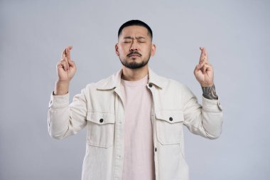 Duygusal Asyalı adamın parmaklarını çapraz yap, bir şeyler dile, rüyalarının gri arka planda gerçek olmasını umut et.