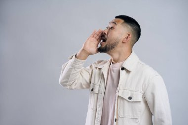 Asyalı bir adam el ele tutuşmuş, satıştan bahsedip bağırıyor. Gri arka planda izole bir şekilde kafasını çeviriyor. Promosyon, alışveriş konsepti           