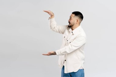 Yakışıklı heyecanlı Asyalı adam el ele tutuşuyor, gri arka planda izole edilmiş bir şey sunuyor, kopyalama alanı. Alışveriş, reklam konsepti.