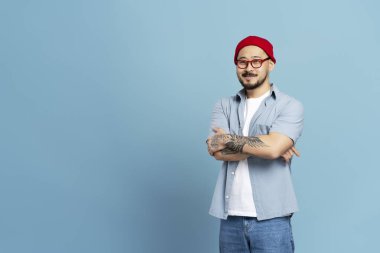 Kolları çapraz gülümseyen Asyalı adam ve stil dövmesi mavi arka planda izole edilmiş, kopyalama alanı.