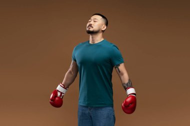 Kırmızı boks eldiveni giyen yakışıklı Asyalı boksörün portresi kahverengi arka planda izole edilmiş bir boks maçına hazırlanıyor. Spor yarışması, motivasyon konsepti